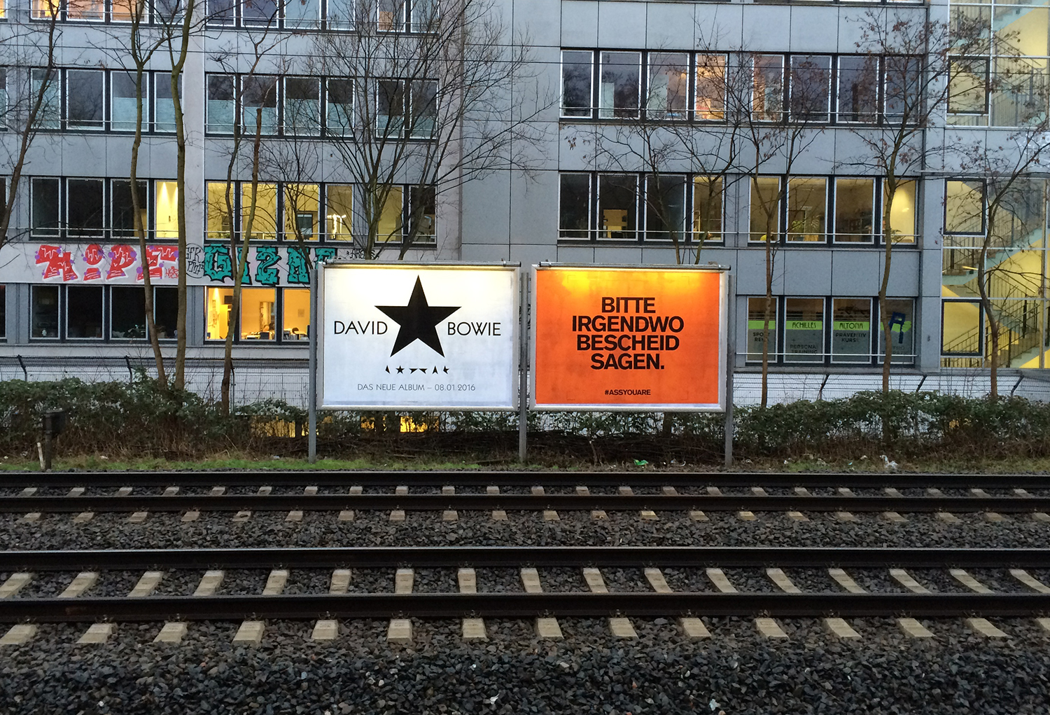 Zwei Plakatwände nebeneinander hinter Bahngleisen