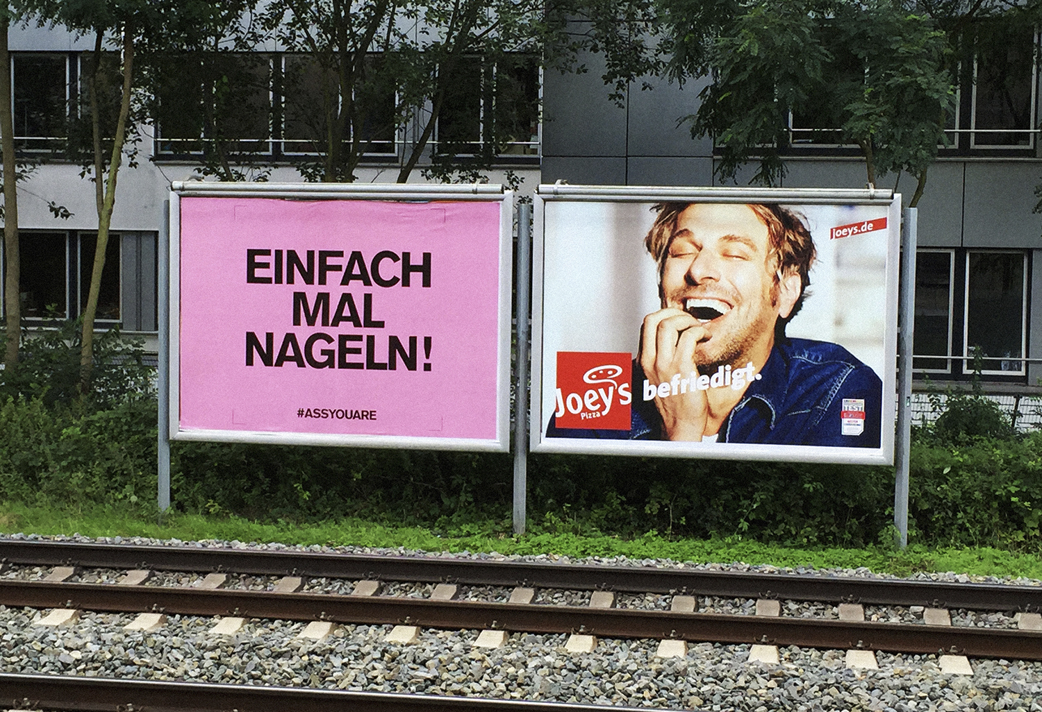 Zwei Plakatwände neben einem Bahngleis auf grünem Rasen