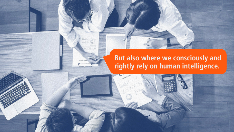 Team meeting with focus on human intelligence in AI use - people discussing documents, an orange speech bubble emphasises that human intelligence is consciously incorporated into the process.